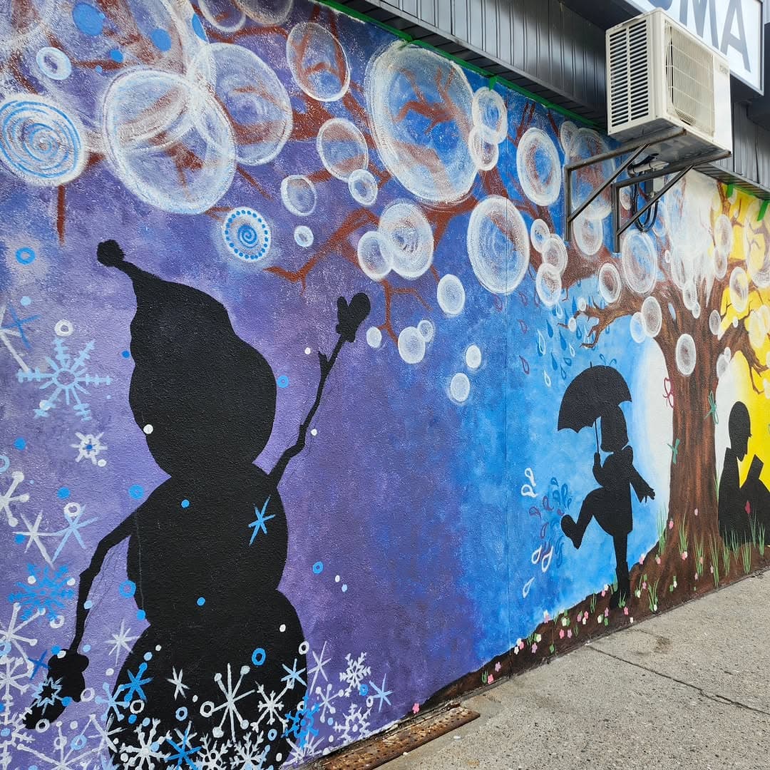 A large outdoor wall mural of children playing through the four seasons, painted by Bronagh Joyce Morgan.